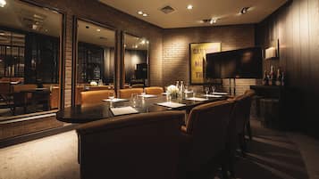 Un área de bar moderna con asientos de cuero, una barra alargada y un televisor de pantalla plana grande montado en la pared.