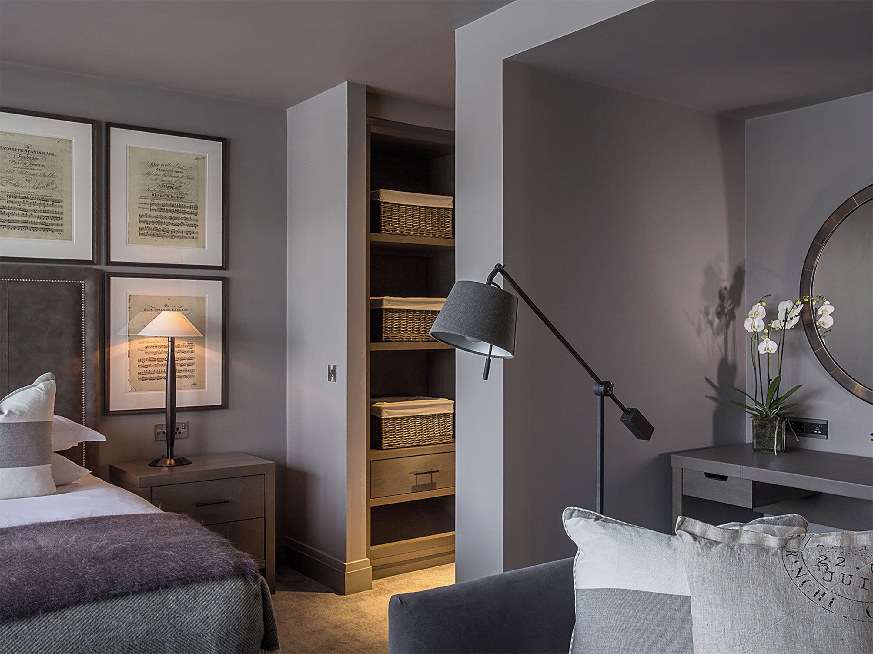 A bedroom with a bed, bedside table, lamp, framed documents, a wardrobe, and a mirror.