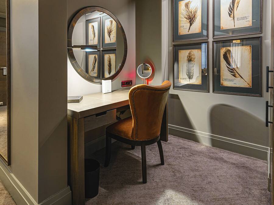 Een studeerkamer met een bureau, stoel en een lijst met een veerillustratie aan de muur.