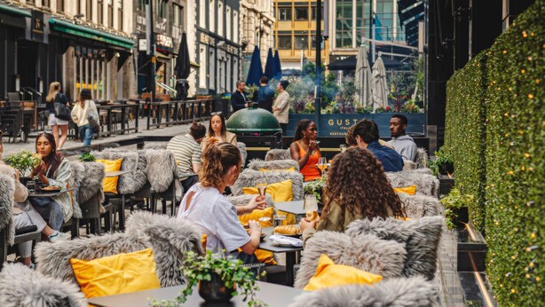 An outdoor café with fur-covered chairs and yellow cushions, surrounded by urban buildings and greenery. - Dakota Leeds (Leeds)