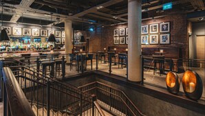 A spacious bar area with multiple seating options, a staircase, and a brick wall with framed pictures. - Dakota Leeds (Leeds)