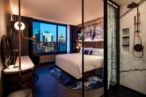 A modern hotel room with a large bed, a desk, a city view, and a shower area. - Hotel EMC2, Autograph Collection (Chicago)