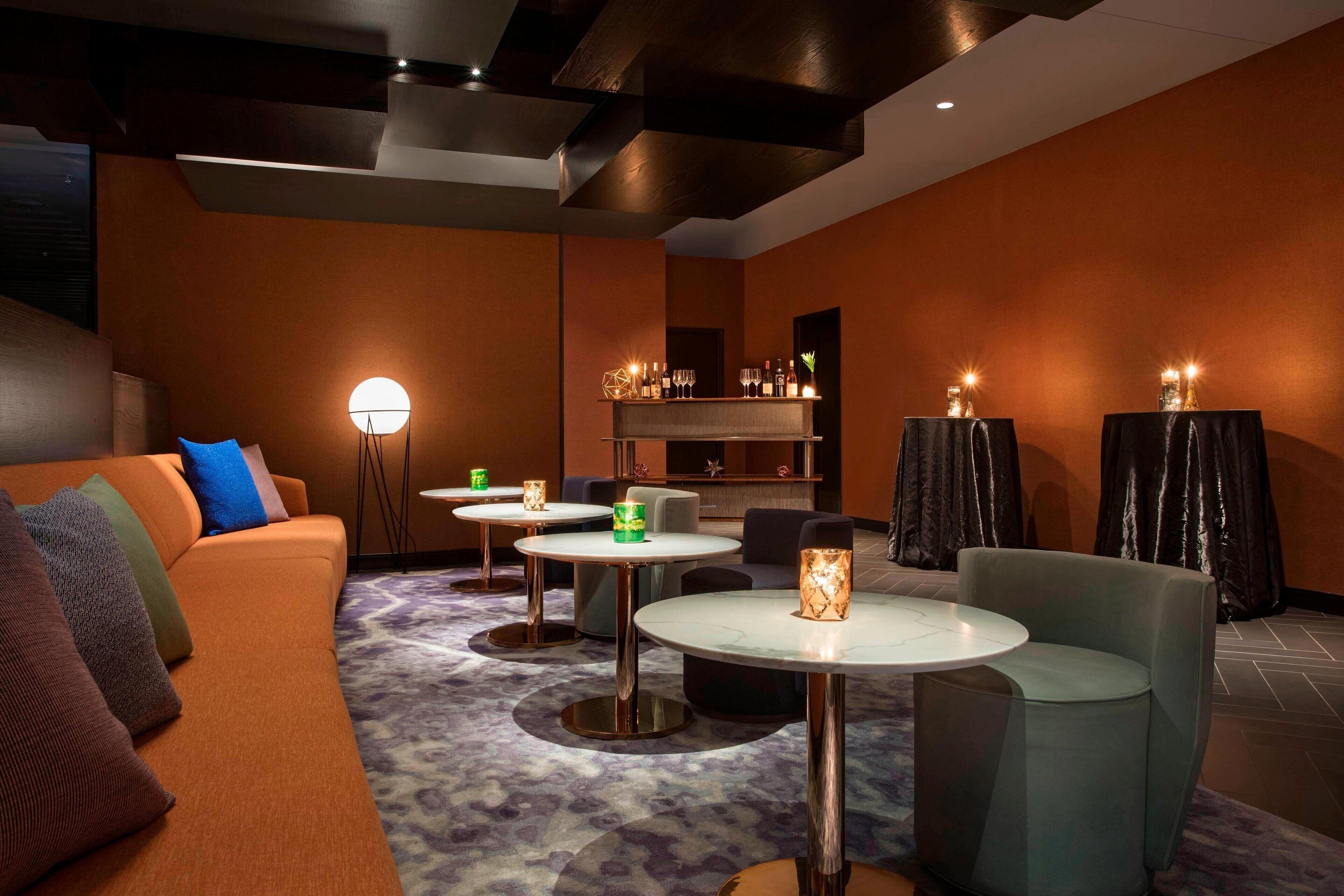 Ein moderner Lounge-Bereich mit einer Couch, runden Tischen und stimmungsvoller Beleuchtung.