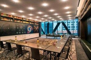 Un salón de conferencias con una larga mesa, sillas y una estantería llena de libros.