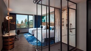 A modern hotel room with a large bed, a desk, and a view of the cityscape. - Hotel EMC2, Autograph Collection (Chicago)
