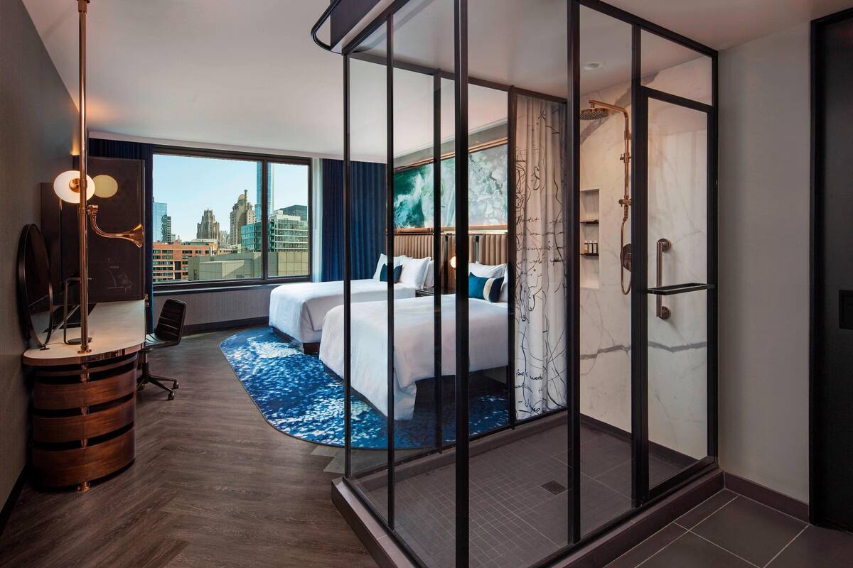 A modern hotel room with a large bed, a desk, and a view of the cityscape.