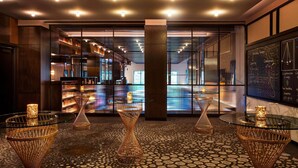 A modern lobby with geometric patterned flooring, glass tables with candles, and a visible bar area with shelves. - Hotel EMC2, Autograph Collection (Chicago)