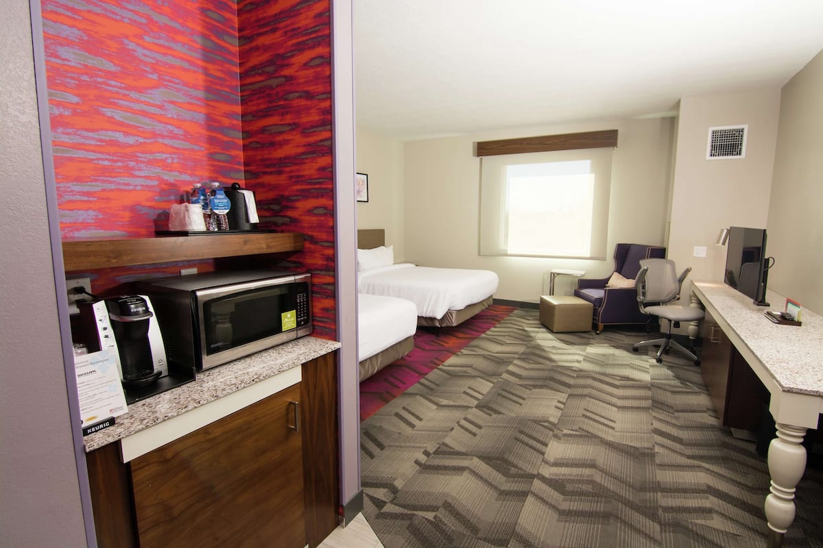 A hotel room with a kitchenette, a bed, a desk, and a chair.