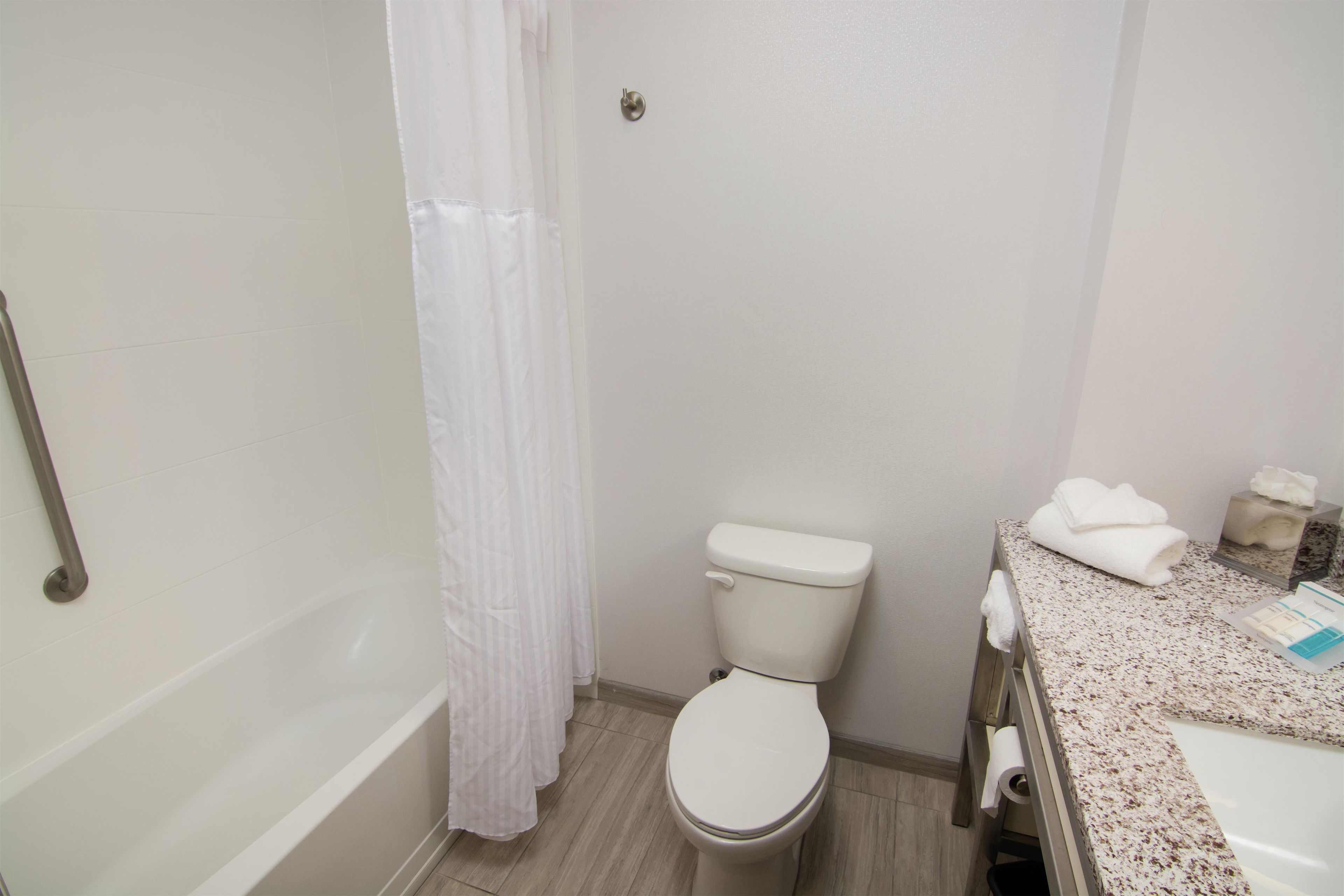 A bathroom with a toilet, a shower curtain, a sink with a towel, and a toilet paper holder.