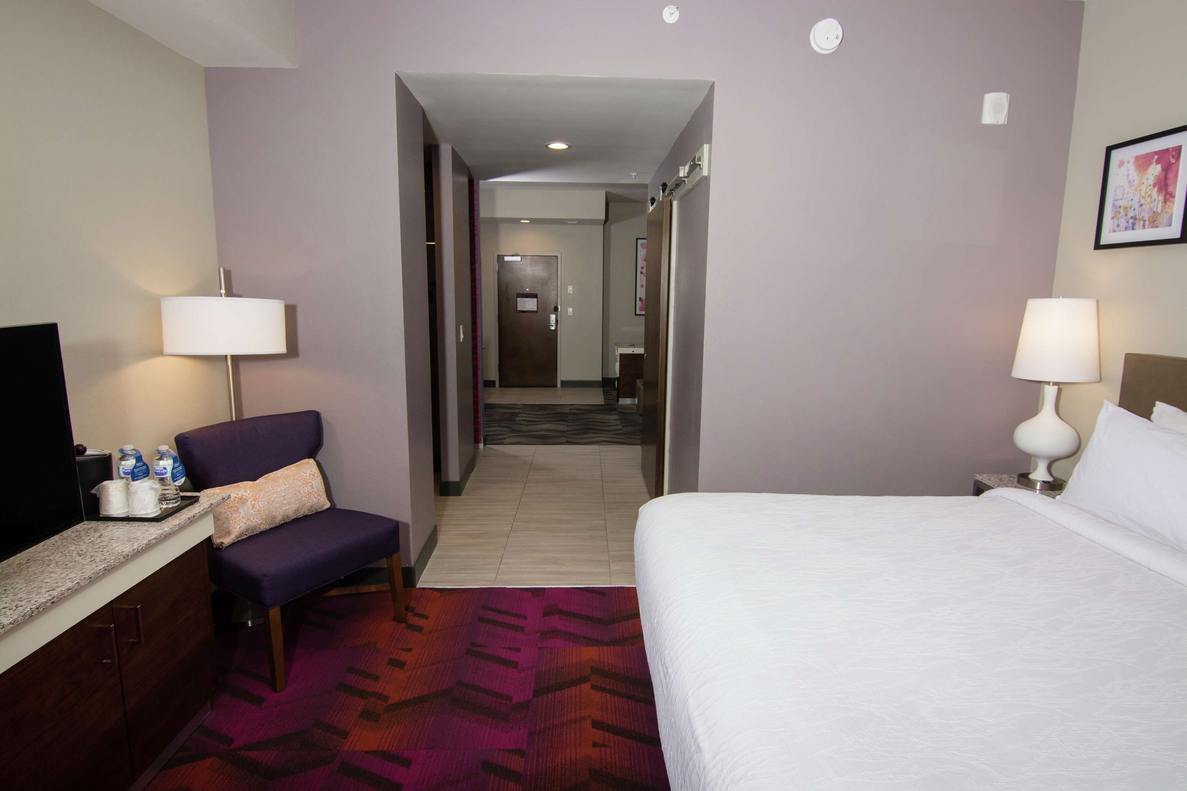 Ein Hotelzimmer mit Bett, Sessel, Schreibtisch mit Fernseher und einem durchgegangenen Tür erkennbaren Badezimmer.