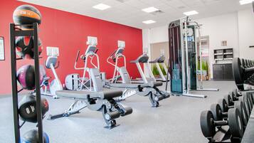 A gym with exercise equipment, a red wall, and a ceiling with lights.