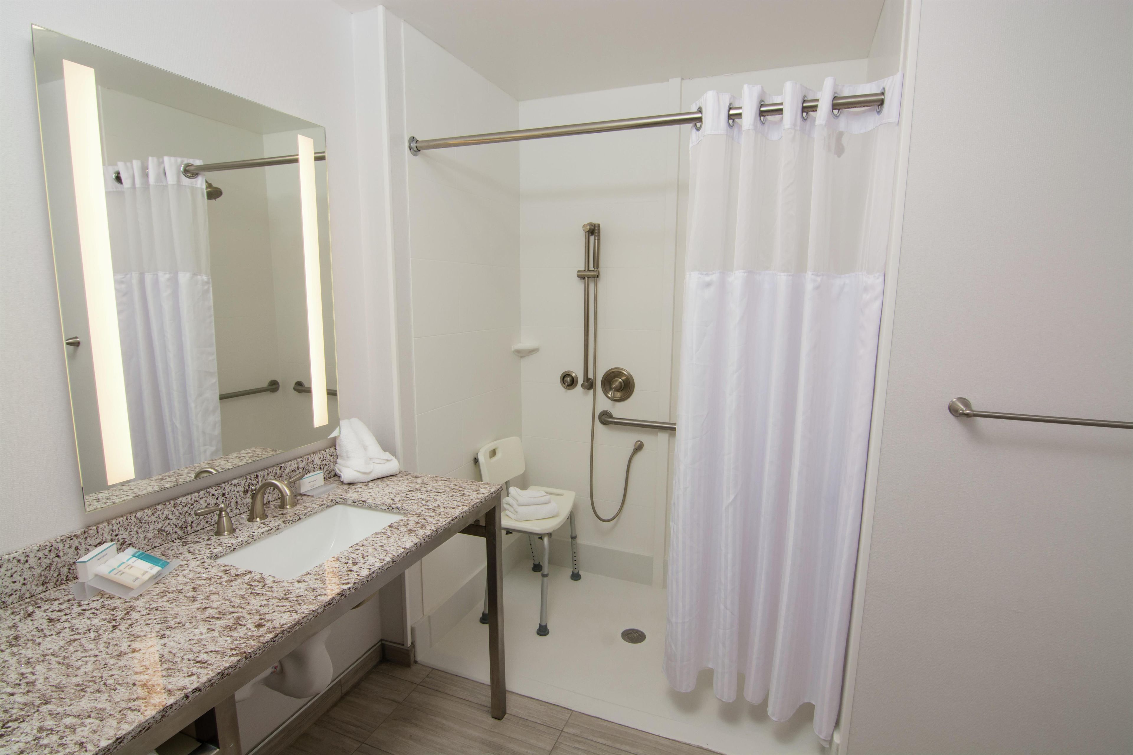 Un baño con lavamanos, espejo, ducha y una toalla blanca.