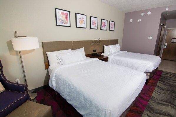 A hotel room with two beds, a nightstand, a lamp, and a chair.