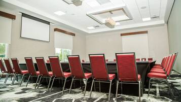 Une salle de conférence avec une longue table, des chaises rouges et un écran de projection.
