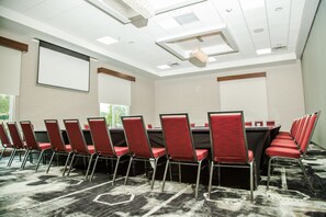 Un salón de conferencias con una larga mesa, sillas rojas y una pantalla para proyector.