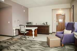 A modern office space with a desk, office chair, kitchenette, and a seating area with a sofa and ottoman.
