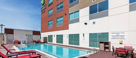 Um Holiday Inn Express & Suites com área de piscina, incluindo cadeiras de descanso e um aviso indicando capacidade para 20 pessoas.