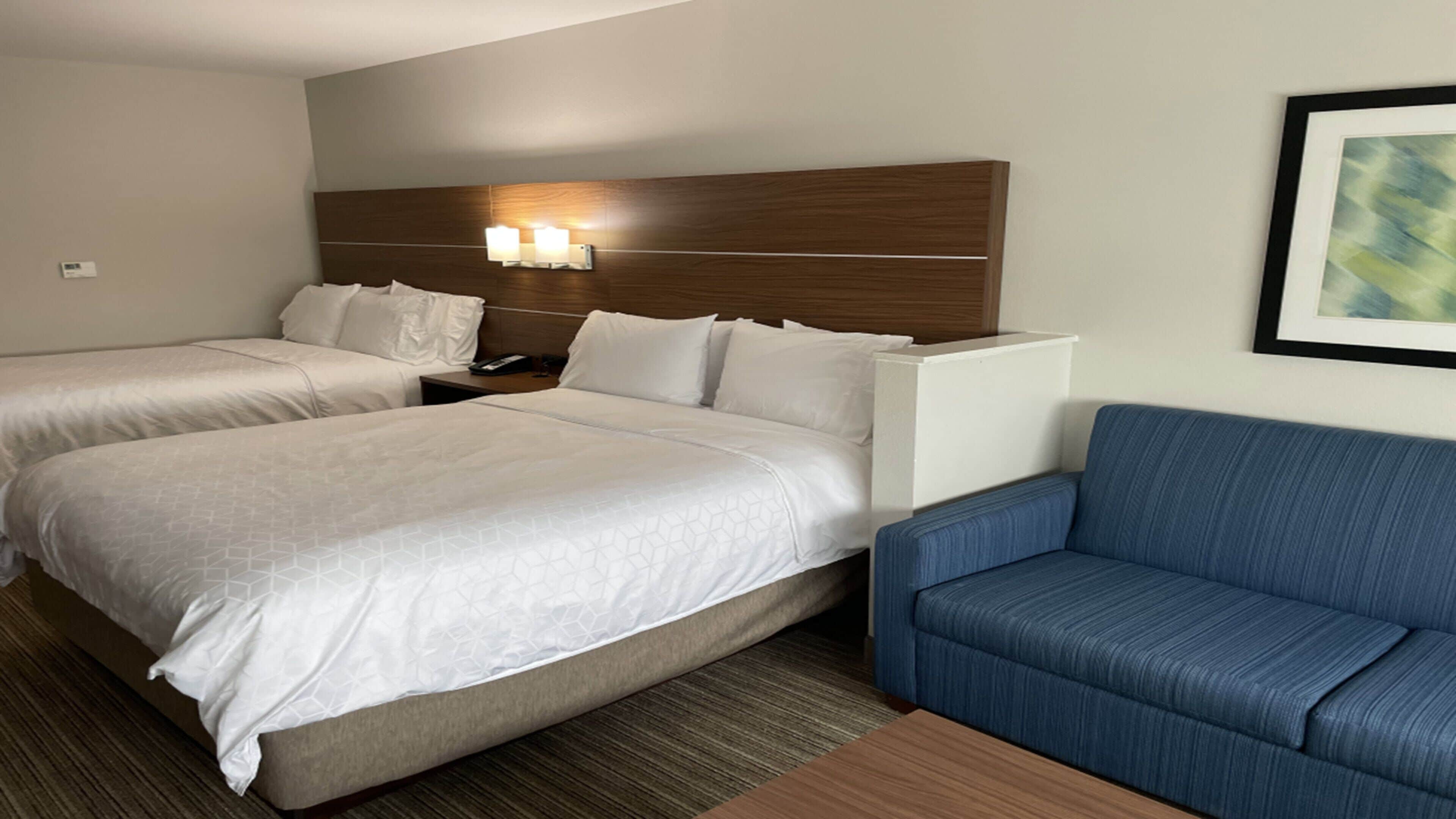 A hotel room with two beds, a blue sofa, and a nightstand with a lamp.