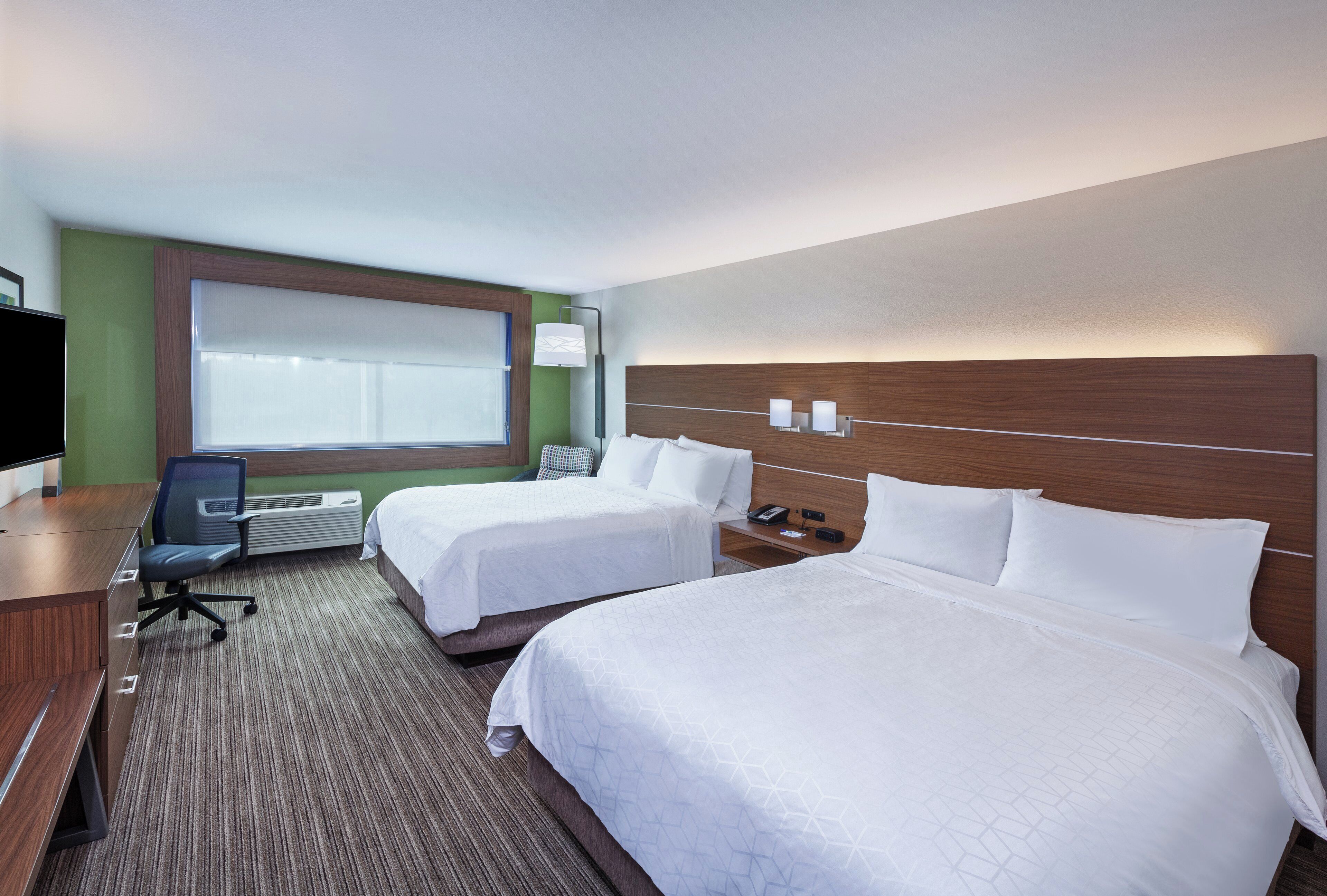 A hotel room with two beds, a desk, a chair, a TV, and a window.