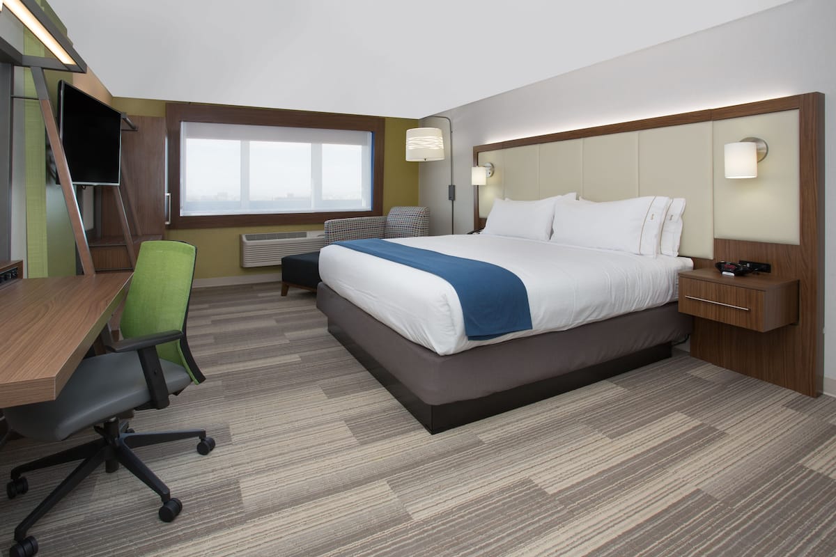 A hotel room with a bed, desk, chair, and a window.