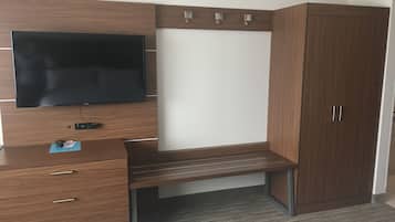 A modern bedroom with a wooden desk, a flat-screen TV mounted on the wall, a wardrobe, and a bedside table.