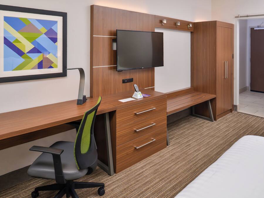 A hotel room with a wooden desk, a flat-screen TV, a chair, a bed, and a framed artwork on the wall.