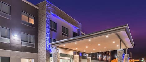 Un hotel moderno con entrada cubierta, fachada de piedra y zona de estacionamiento.