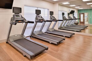 A row of treadmills in a gym with a large mirror and a TV screen on each treadmill.