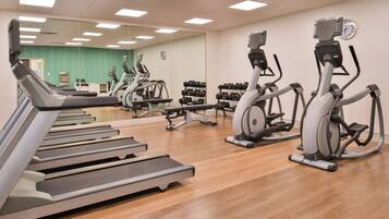 Un gimnasio con varias cintas de correr, elípticas y un estante con mancuernas.