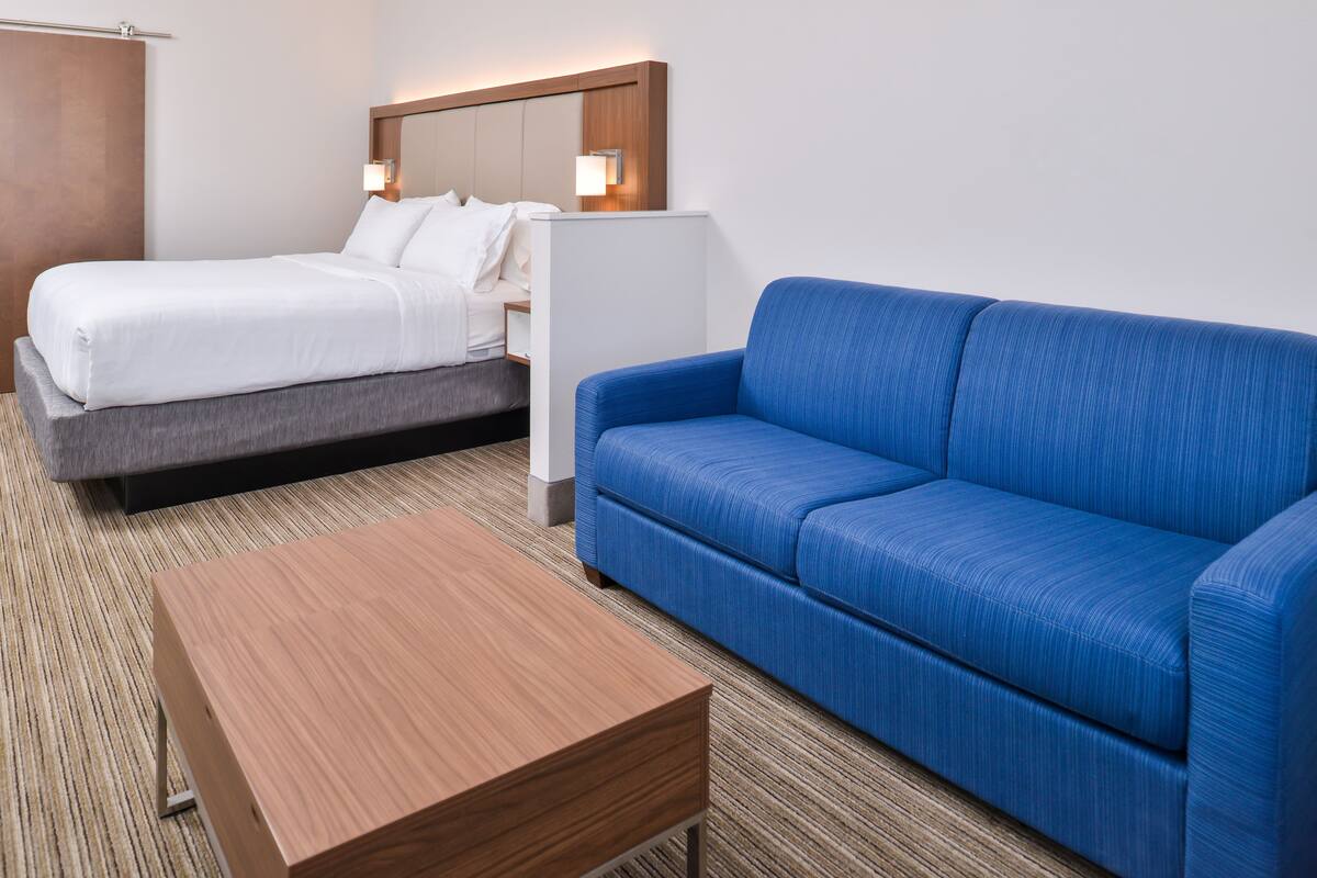 A hotel room with a bed, a blue sofa, and a wooden table.