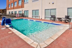 A swimming pool with blue tiles, a hot tub capacity sign, and outdoor seating.
