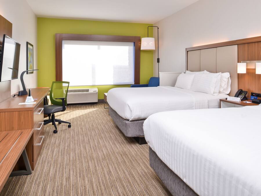 A hotel room with two beds, a desk, a chair, a TV, and a window with blinds.