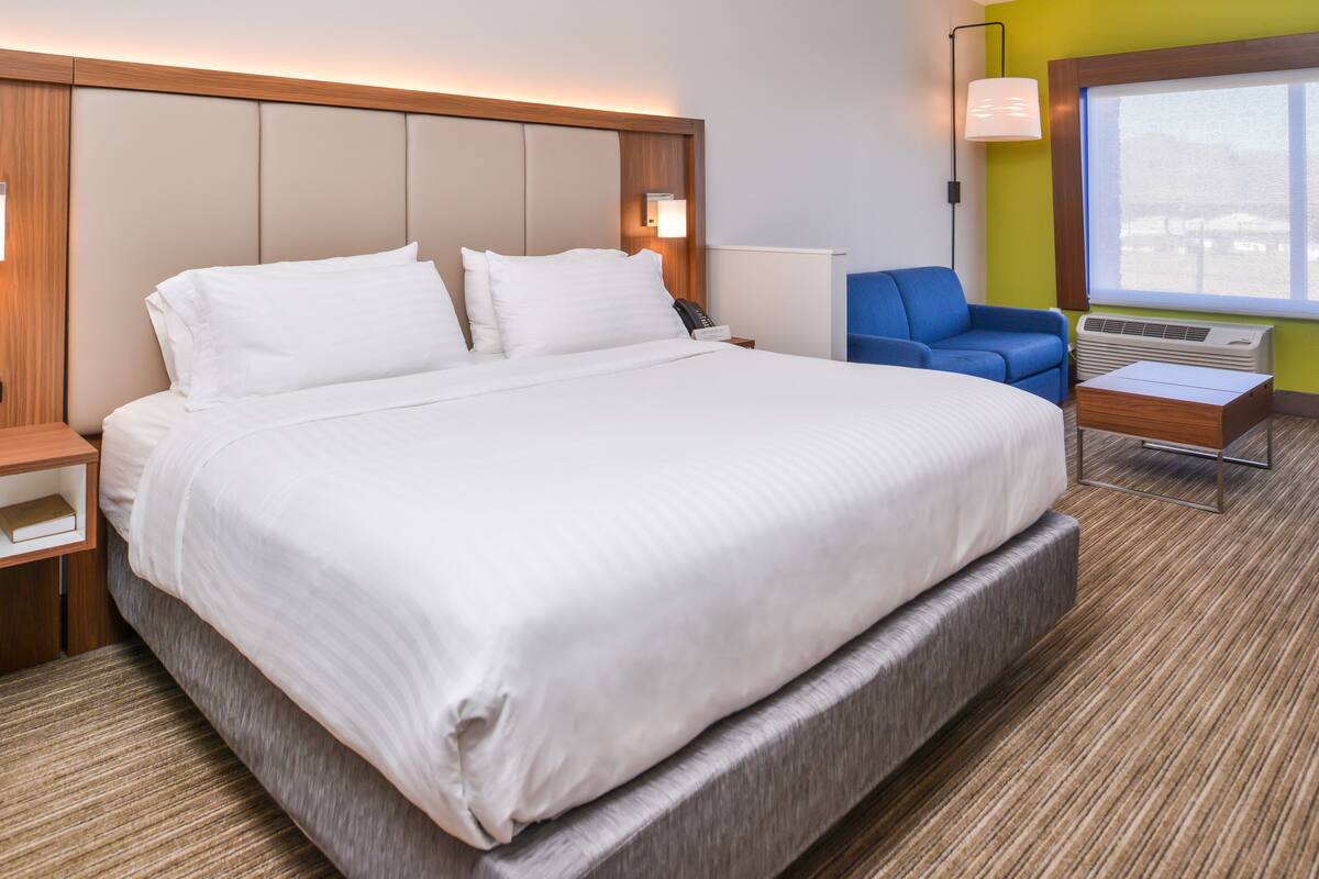 A hotel room with a large bed, a desk, a chair, and a window.