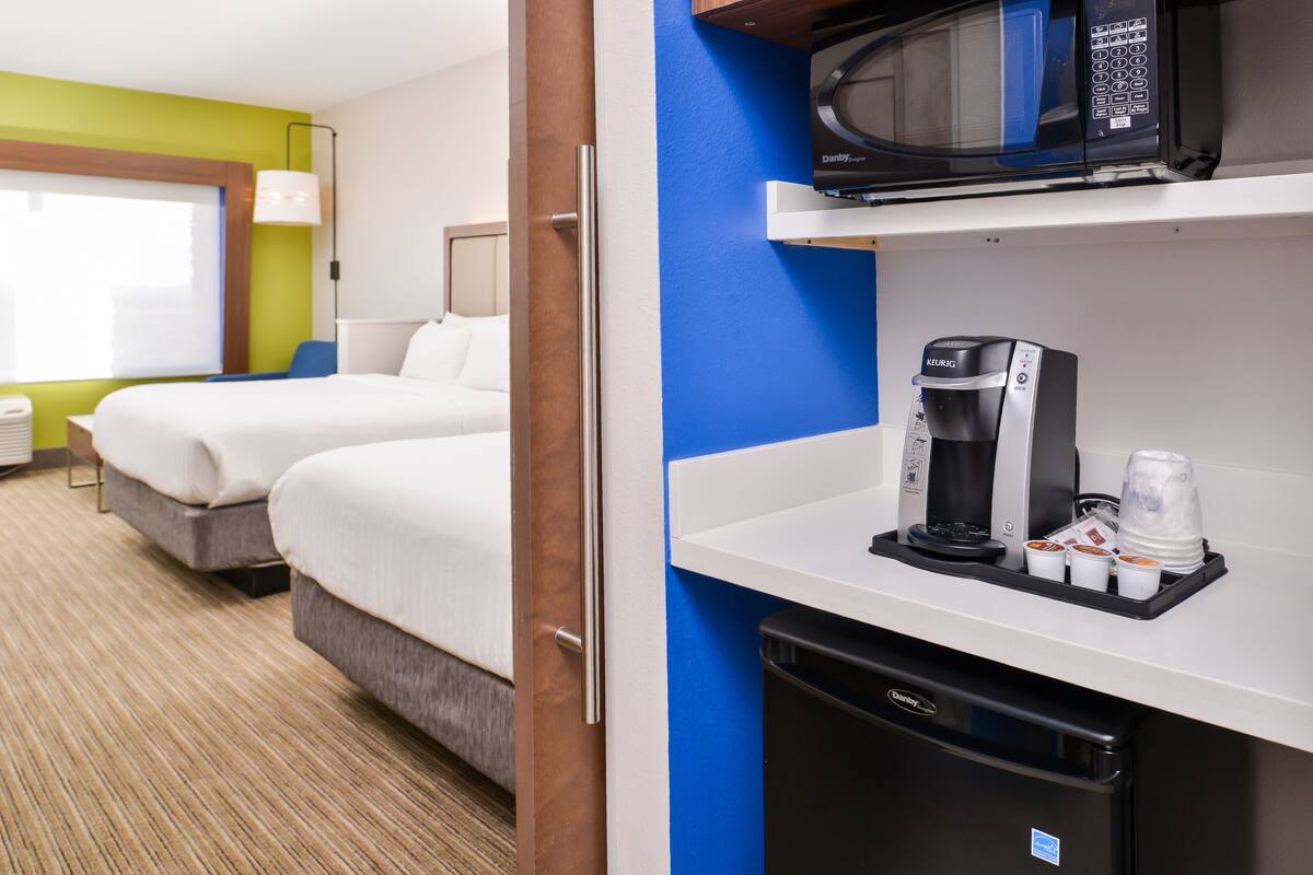 A hotel room with two beds, a microwave, a coffee maker, and a trash bin.
