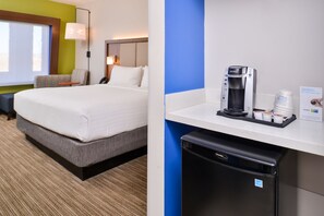 A hotel room with a bed, a desk with a coffee maker, and a trash bin.