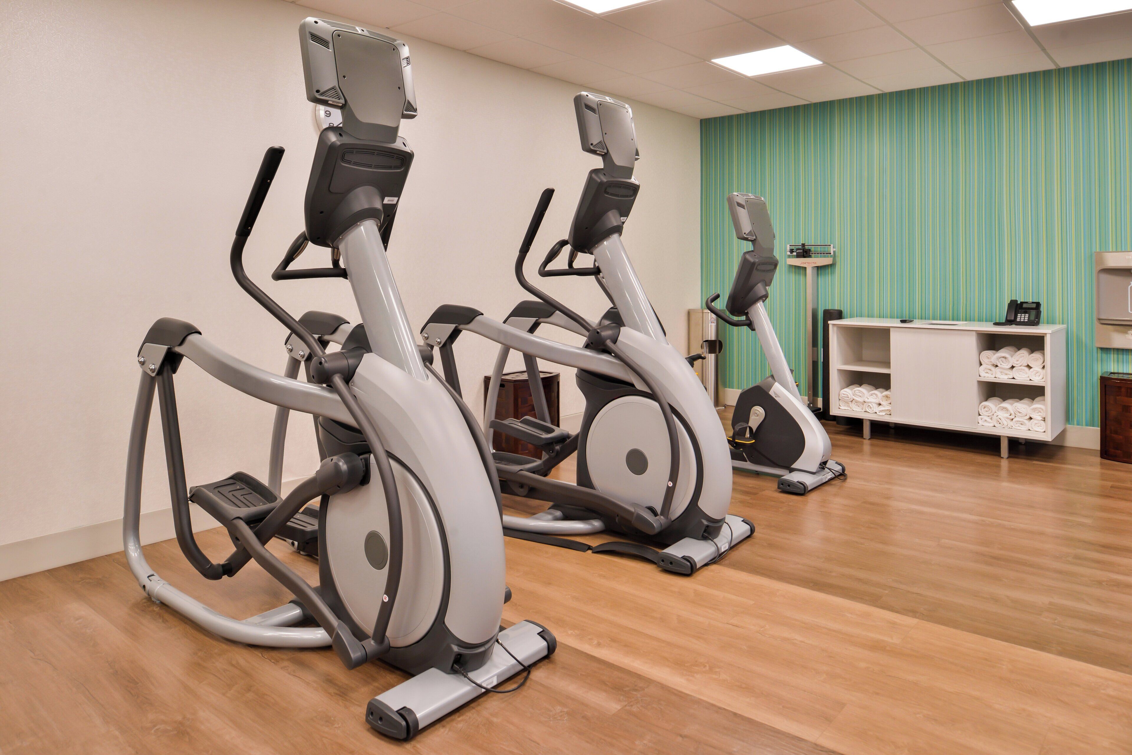 A fitness room with three stationary bikes, a reception desk, and a wall with a striped pattern.