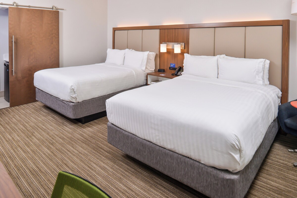 A hotel room with two beds, a wooden headboard, a nightstand with a phone, and a desk with a chair.
