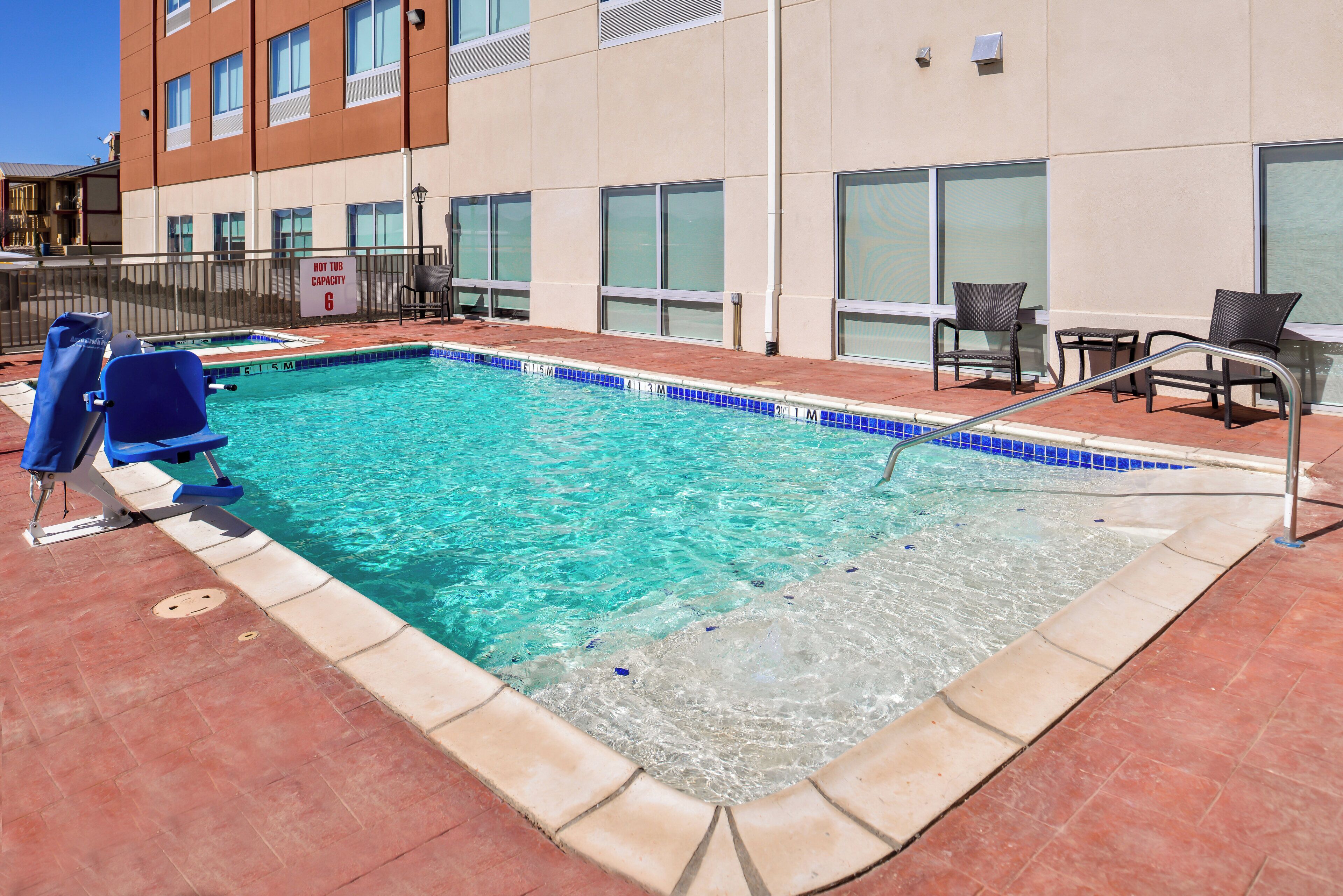 A swimming pool with a hot tub capacity sign, lounge chairs, and a tiled deck.