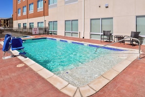A swimming pool with a hot tub capacity sign, lounge chairs, and a tiled deck.