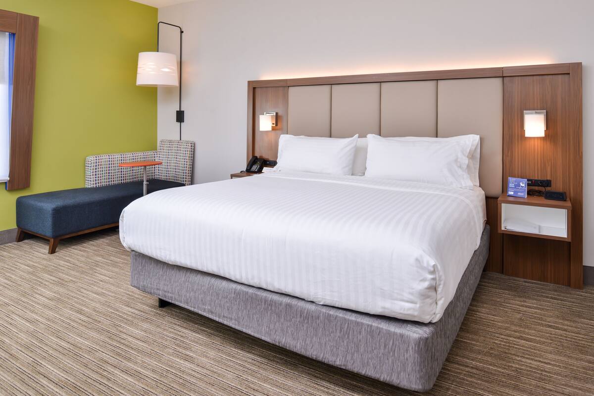 A hotel room with a large bed, a bedside table with a lamp, a small desk, and a chair.