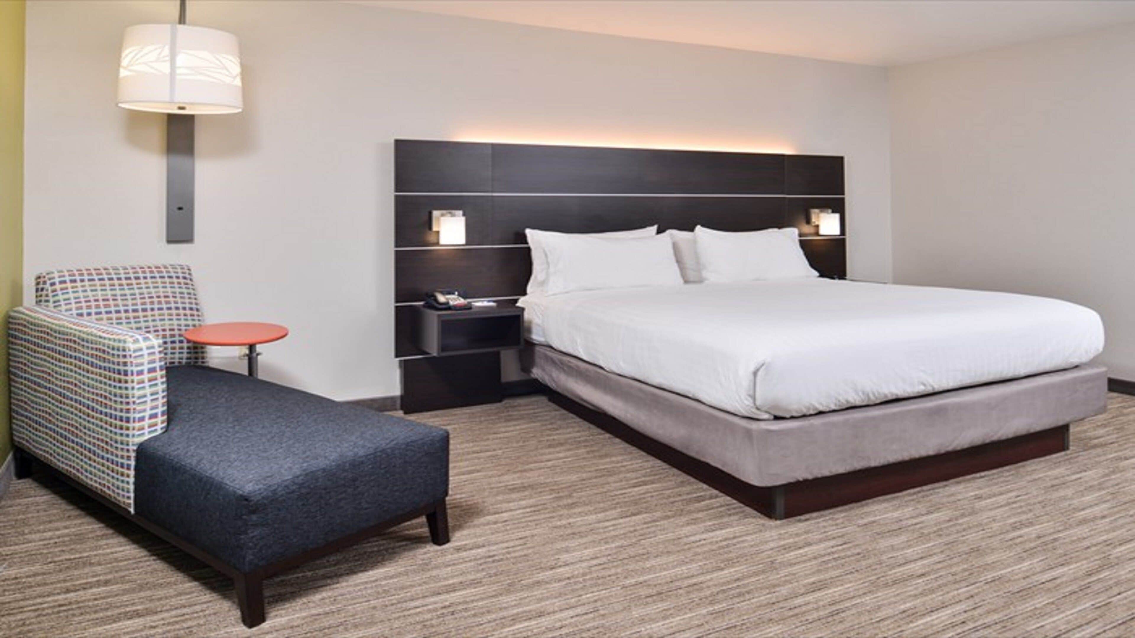 A hotel room with a bed, a chair, a small table, and a nightstand.