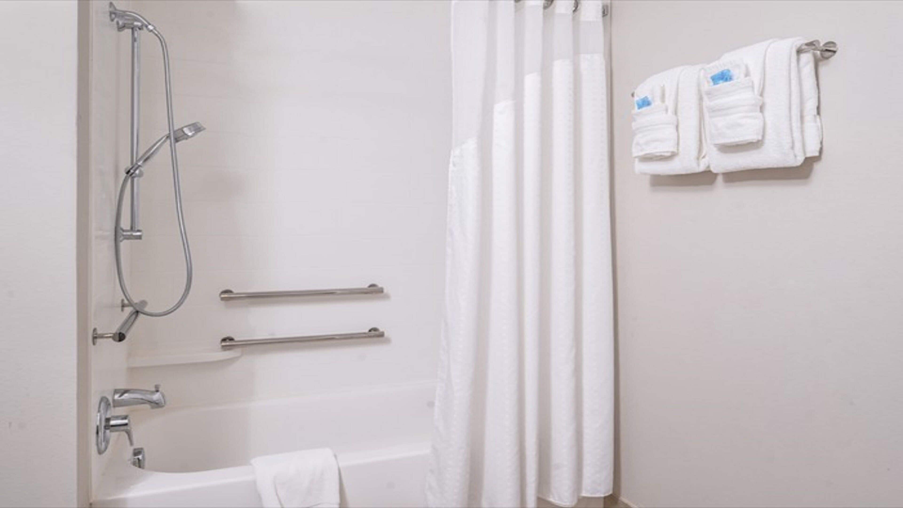 A bathroom with a bathtub, a shower with a handheld showerhead, grab bars, and a towel rack with towels.
