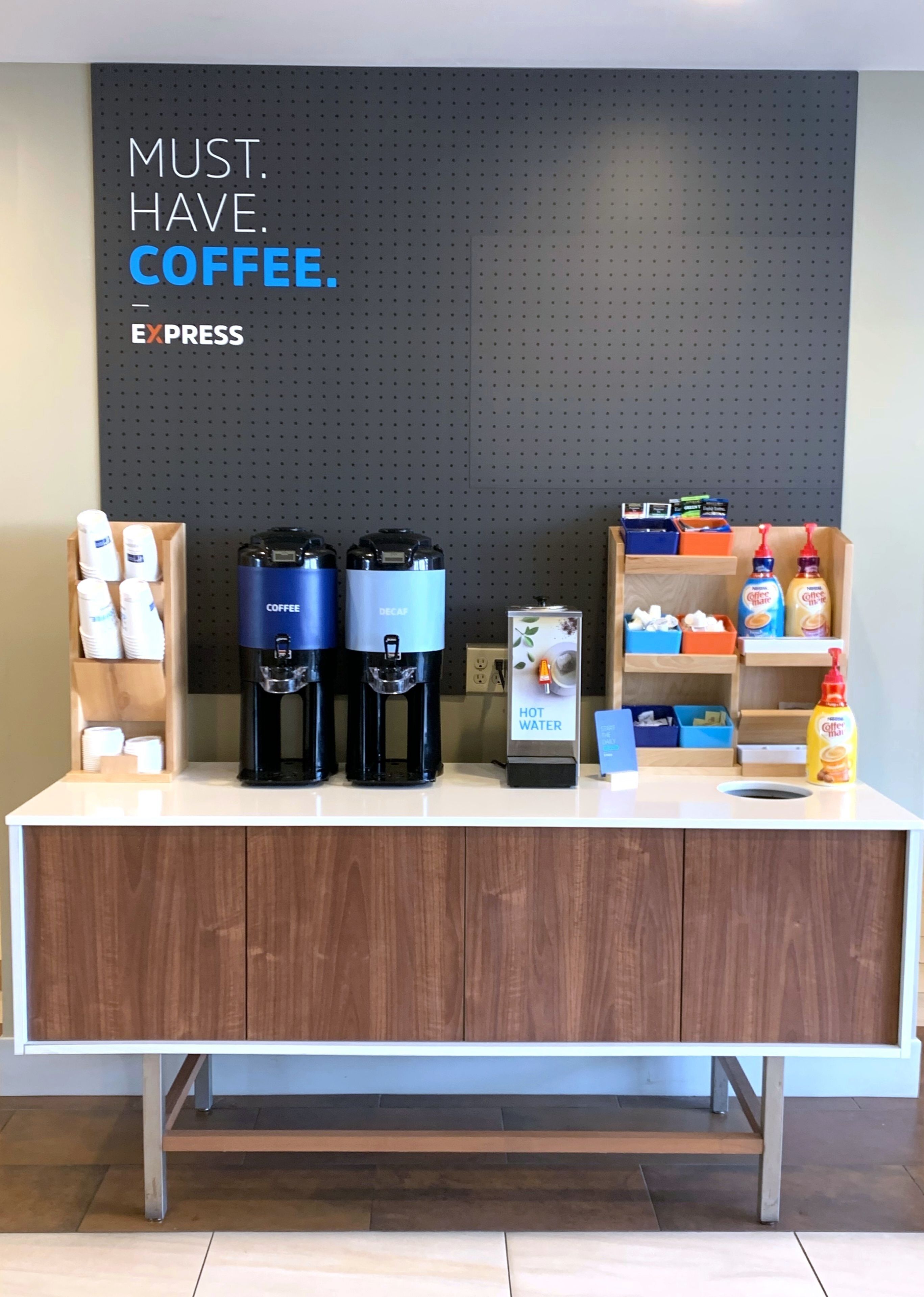 A coffee station with two coffee makers, a water dispenser, and various coffee and creamer dispensers.