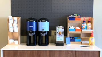A coffee station with two coffee makers, a water dispenser, and various coffee and creamer dispensers.