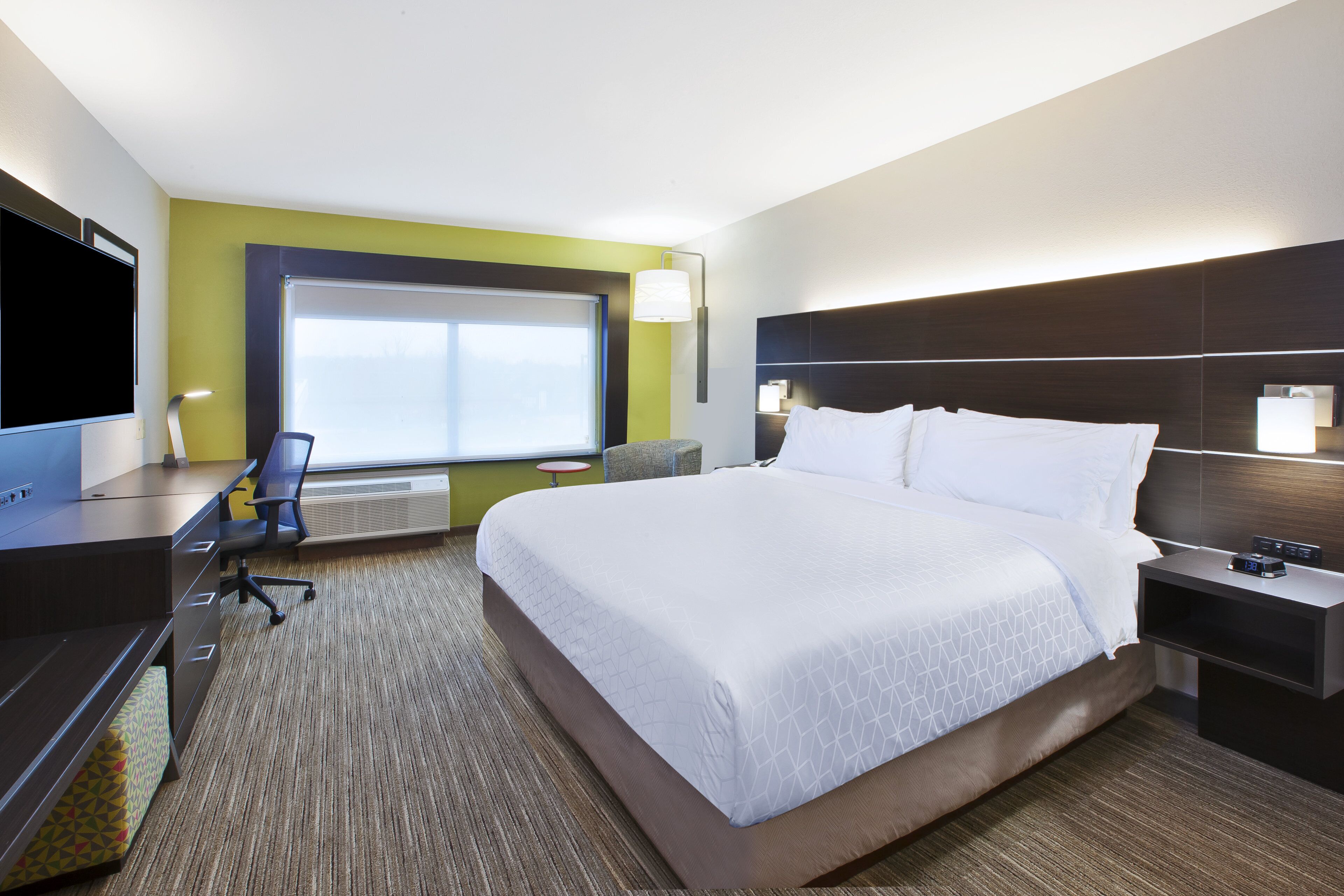 A hotel room with a large bed, a desk, a chair, a TV, and a window.