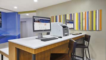 Een receptiebalie met een computer, printer en toetsenbord. Er staat een stoel en er is een muur met verticale strepen.