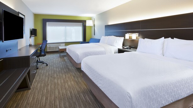 A hotel room with two beds, a desk with a TV, a chair, and a large window.