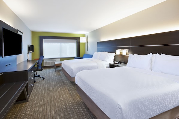 Habitación de hotel con dos camas, un escritorio con televisor, una silla y un ventanal grande.