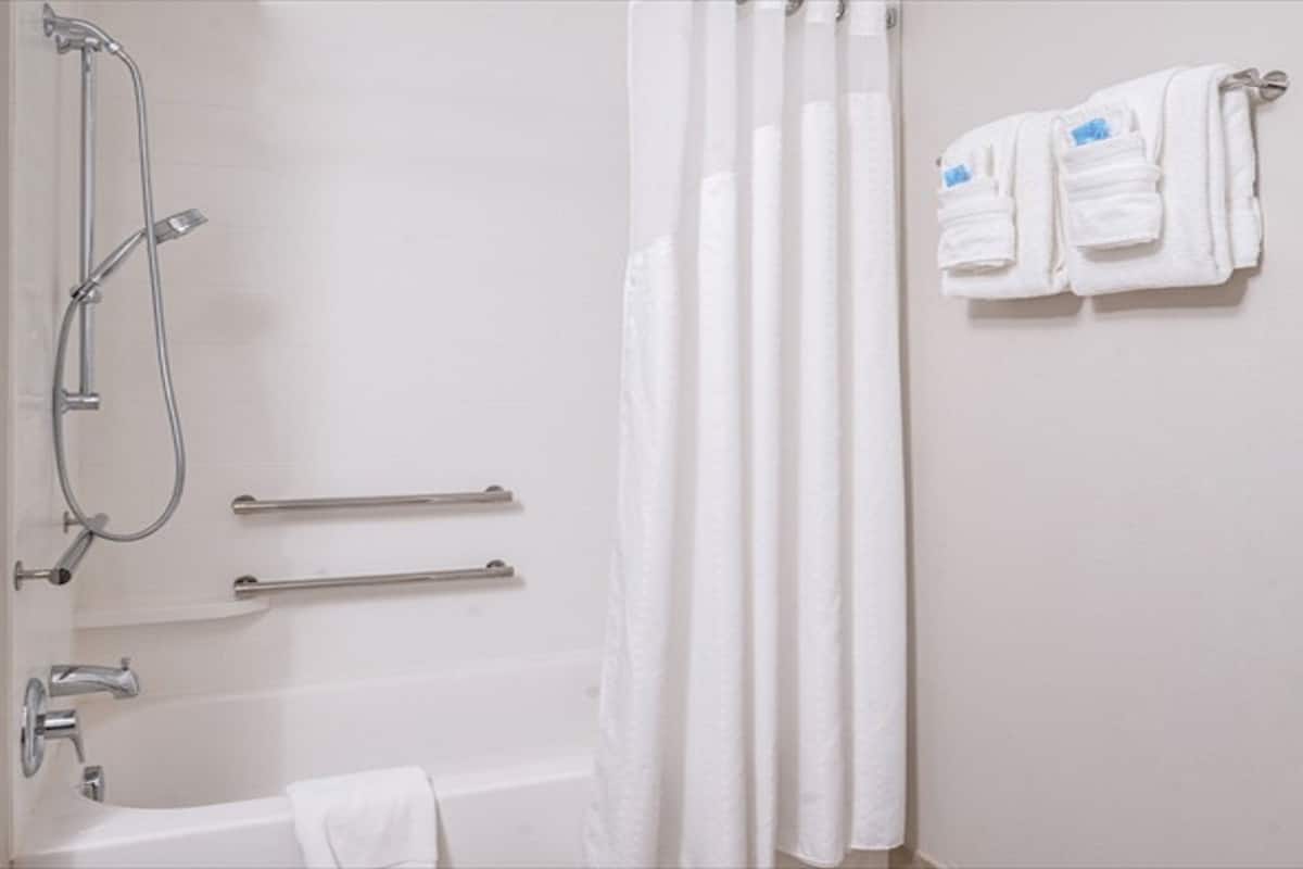 A bathroom with a bathtub, a shower with a handheld showerhead, grab bars, and a towel rack with towels.