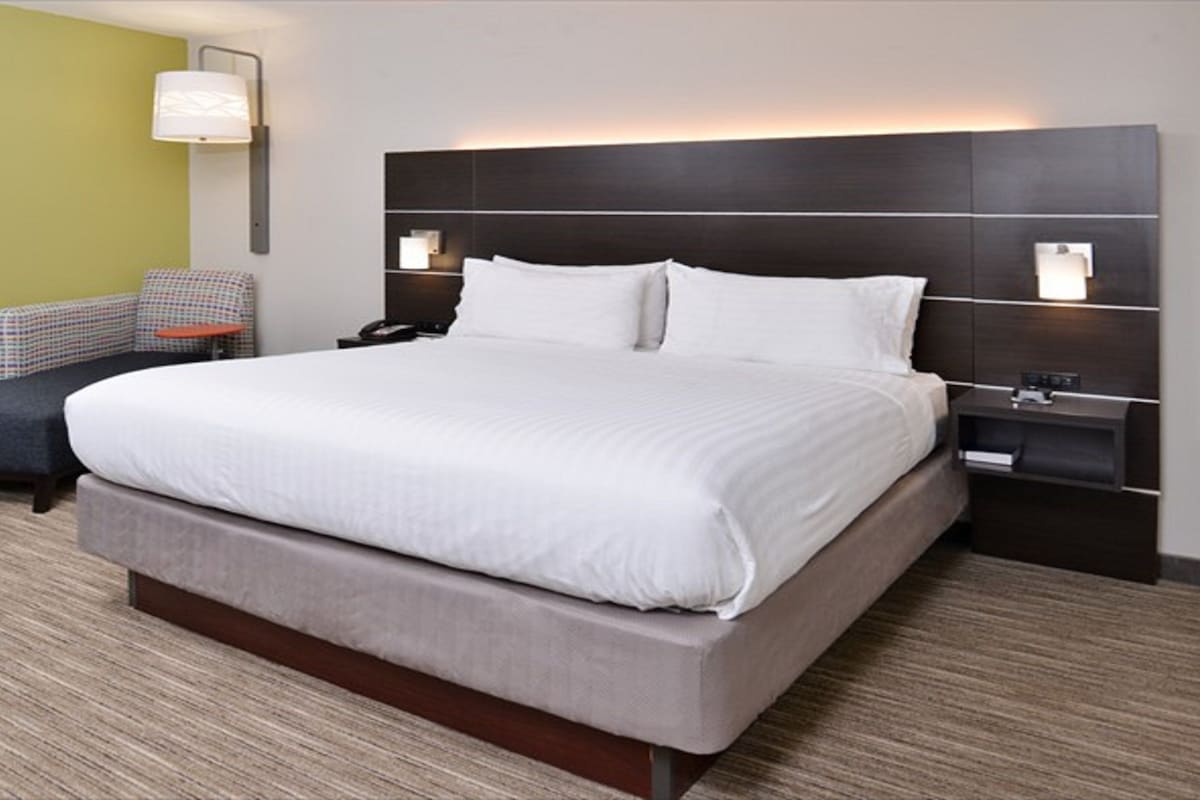 Habitación de hotel con una cama grande, dos mesitas de noche, una silla y una lámpara de pared.